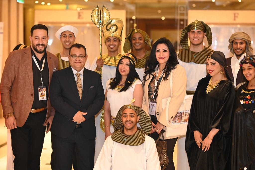 Delegates smile alongside hosts in pharaonic costume, including one holding a gold sceptre, and others in colourful traditional dress.