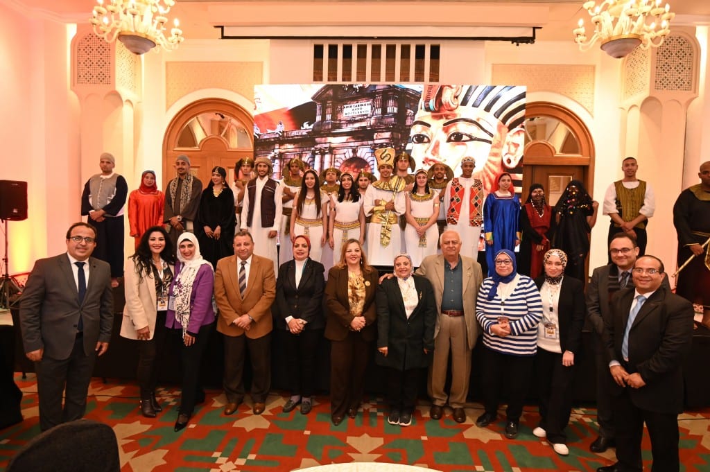 Delegates stand for a group photo in front of performers in pharaonic and traditional costume, backed by a large mural of a pharaoh's mask.